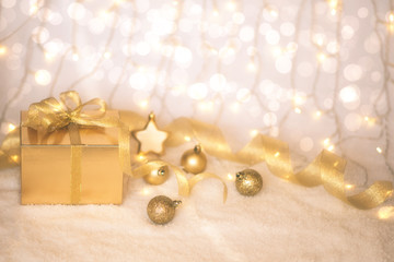Gold Christmas background of defocused twinkling lights with gold balls, decoration and gift box. Selecnive focus. Toned image with copy space for your text.