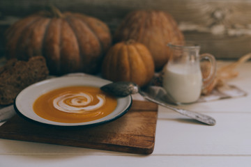 Homemade autumn butternut squash soup with bread. Roasted pumpkin and carrot soup with cream and pumpkin seeds on white wooden background. Concept of healthy eating food. Copy space. Toned image.