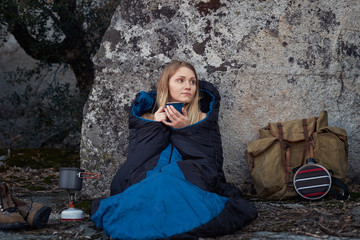 Young woman sitting up in a sleeping bag drining coffee while on a backpacking trip