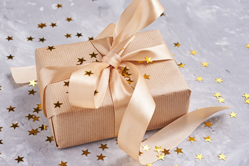 Gift box wrapped in kraft paper with golden bow and confetti in shape star, close up