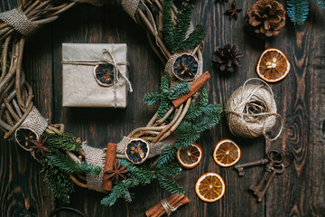 Christmas gifts composition. Wreath made of christmas tree branches and dry ivy on dark vintage wooden board. Christmas background with decorations and gift boxes. Flat lay, top view with copy space.