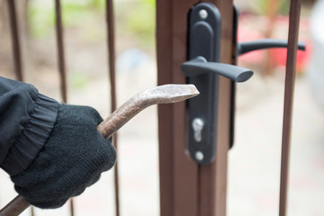 Burglar trying to break the gate with a crowbar. Burglar trying to force a lock using a crowbar