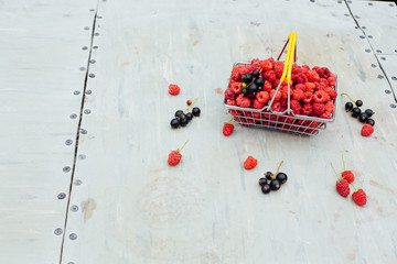 Mini shopping basket full of fresh red ripe raspberry and blackberry on vintage background