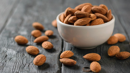 White ceramic bowl with almonds on black rustic table.