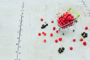 Mini shopping basket full of fresh red ripe raspberry and blackberry on vintage background