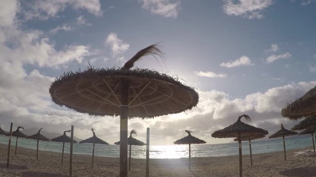 vistas de unas sombrillas de playa con el sol sobre el horizonte en una playa de  mallorca