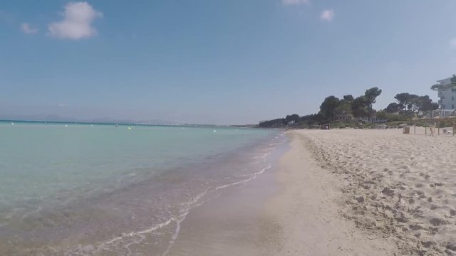 andando por la orilla de la playa en mallorca en un dia soleado con el mar en calma y las olas rompiendo en la orilla