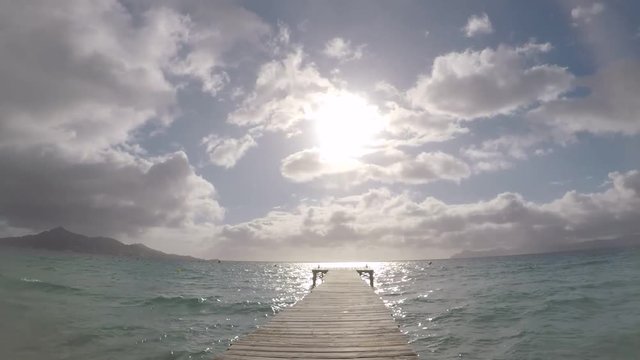 Caminando por un muelle de la playa de muro en mallorca con vistas al horizonte y con el sol saliendo y nubes