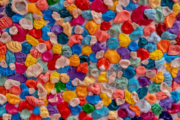 Fototapeta na wymiar A lot of multi-colored chewing gums pasted on the wall creates a uniform texture.
