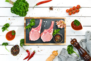 Raw pork steak on the bone. On a stone board with spices and herbs. Top view. Free space for your...