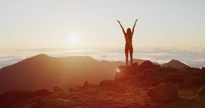 Beautiful young woman performing a spiritual yoga pose on the top of a mountain at sunrise in slow motion, sunrise zen wellness