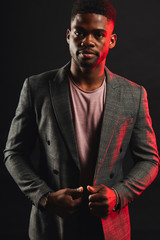 Successful young dark-skinned entrepreneur in formal clothing, standing against dark purple background, thinking and making plans for future, while relaxing after hard day in the office