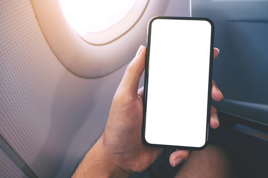 Mockup image of a hand holding a black smart phone with blank desktop screen next to an airplane window
