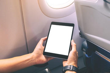 Mockup image of a man holding and looking at black tablet pc with blank white desktop screen next to an airplane window