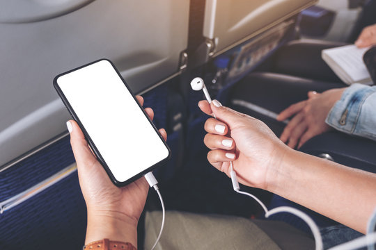 Mockup image of woman's hand holding a black smart phone with blank desktop screen and earphone in cabin