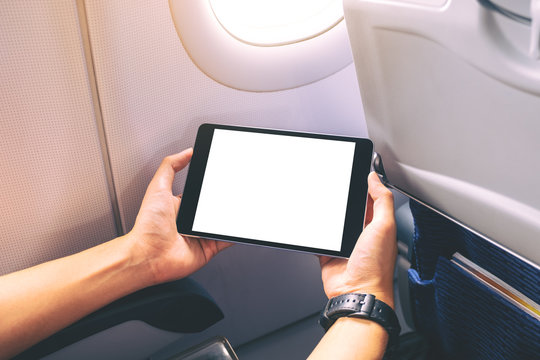 Mockup image of a man holding and looking at black tablet pc with blank white desktop screen next to an airplane window
