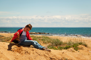 Fototapeta na wymiar Teenager sits on the sand by the sea