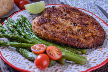 Hot appetizing schnitzel with crispy crust on a plate next to asparagus, lime and cherry tomatoes...