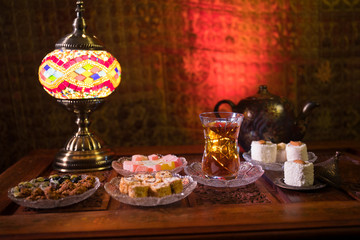 Arabian tea in glass with eastern snacks on vintage wooden surface. Eastern tea concept. Low light lounge interior with carpet. Empty space.