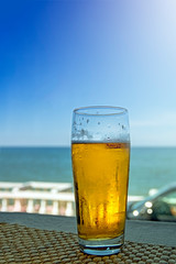Misted glass of beer in the beach bar on the background of the sea landscape. Sunny hot day, afternoon.