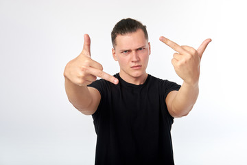 Young attractive man wearing black shirt showing fuck you sign over white wall background.