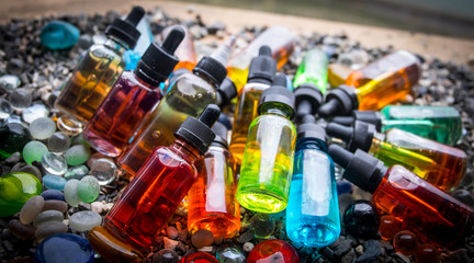 Vape concept. Beautiful colorful vape liquid glass bottles outdoor on stones. Useful as background or electronic cigarette advertisement.