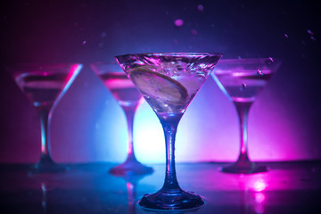 Martini cocktail glass in hand splashing on dark toned smoky background or colorful cocktail in glass with splashes and olives. Party club entertainment. Mixed light. Selective focus