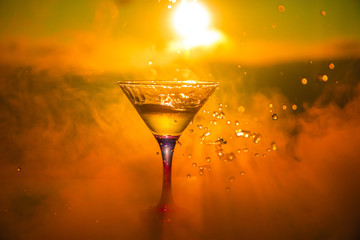 Martini cocktail glass in hand splashing on dark toned smoky background or colorful cocktail in...