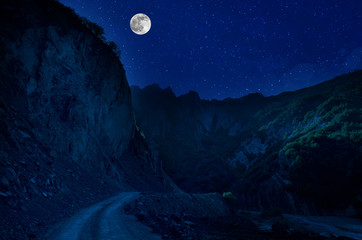 Mountain Road through the forest on a full moon night. Scenic night landscape of country road at night with large moon. Long shutter photo