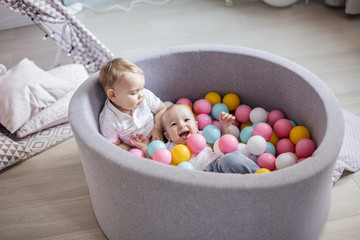 Two adorable 1 -year old male infants playing with colorful balls in soft playpen placed on children playground at indoor play center. Activity toys for little kid. Happy Childhood.