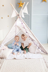 Fototapeta na wymiar Couple of small infant boys of 1-year old playing alone in teepee tent with garland at nursery in home interior.