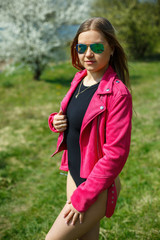 Girl in a black bodysuit and a pink jacket in nature with a flowering tree