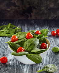 Spinach and cherry tomatoes in white bowl on wooden table