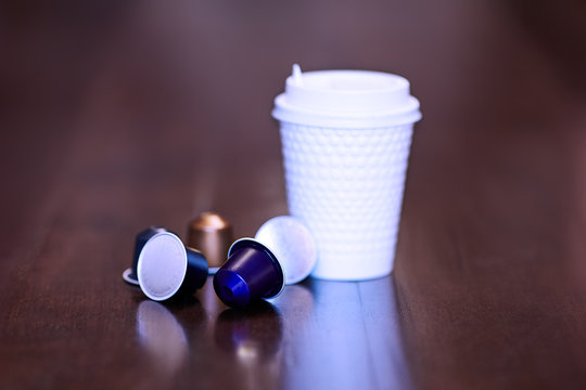 Close up picture of white plastic coffe cup with some colorful replaceable cartridges with coffee. Indoors, copy space, copy atmosphere, selective focus.