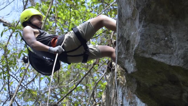 Good looking asian guy rappelling himself from the cliff at jungle. extremely dangerous from the high but safety with equipment.