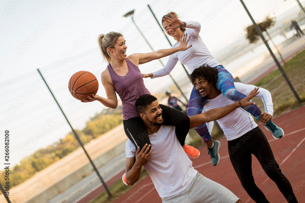 Wall mural young women sitting on the men shoulders and holding a basketball at outdoor court