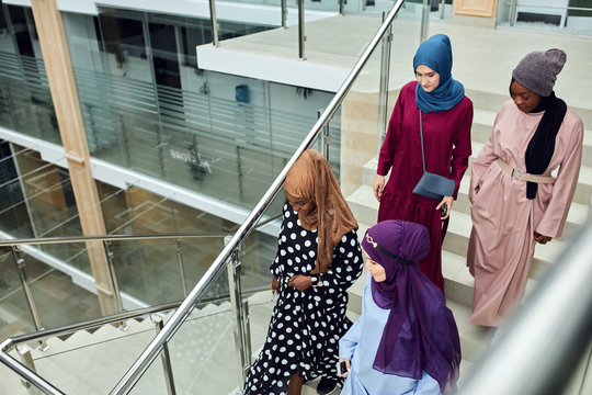 Multicultural group of female Arabian students, dressed in national dresses and scarfs going down the stairs of university , sharing ideas with each other on the way