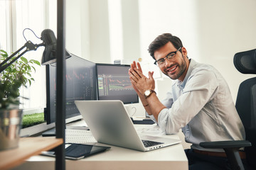 Young and successful. Happy bearded trader in formal wear and eyeglasses looking at camera and smiling while sitting in his modern office.