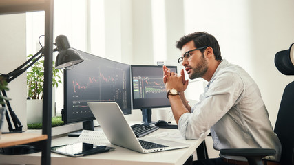 Trading strategy. Successful young trader in eyeglasses looking at analyzing trading charts on...