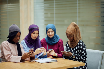 Asian Islamic women in bright hijabs sharing info from smartphone during their visit a seminar at education centre