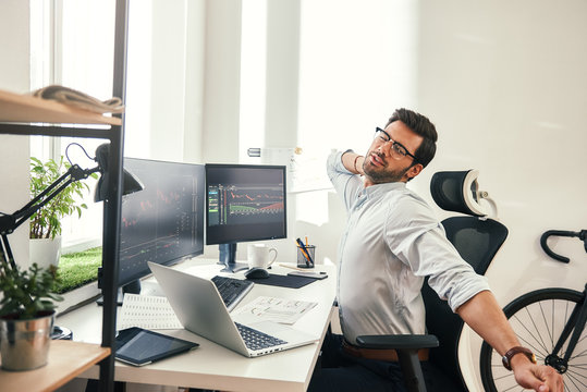 Feeling exhausted. Tired young beard businessman or trader in formal wear keeping eyes closed and stretching while sitting at his working place