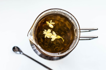 green tea with jasmine flowers infuse in a teapot; three jasmine flowers float on the tea surface; view from above; transparent; clarity