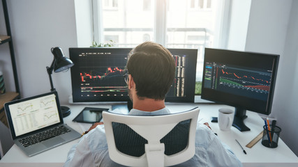 Trading stocks online. Back view of young businessman or trader working with graph and charts on...