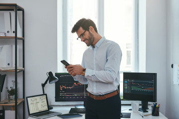 Modern business. Happy and successful trader in formal wear is looking at trading graphs and...