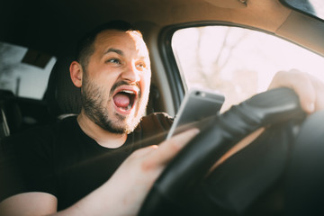 Young man sitting in his car screaming distracted by smartphone