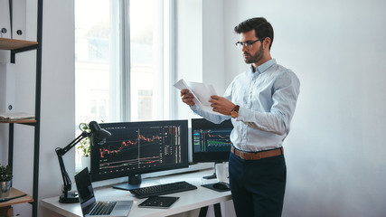 Analyzing data. Thoughtful trader in eyeglasses holding a financial report and analyzing trading...