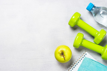 Dumbbells, measuring tape, water and apple top view.
