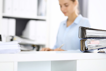 Binders with papers are waiting to be processed by business woman or bookkeeper back in blur....