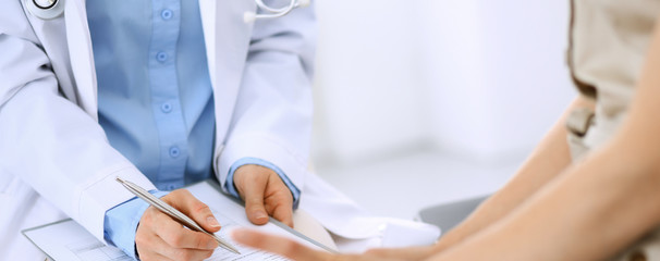 Doctor and patient talking. Physician at work in hospital while writing up medication history records form on clipboard near sitting woman. Healthcare and medicine concepts