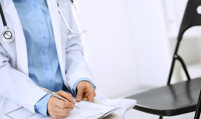 Female doctor writing up medication history records form on clipboard, while sitting at the chair. Physician at work in hospital or clinic. Healthcare, insurance and medicine concept